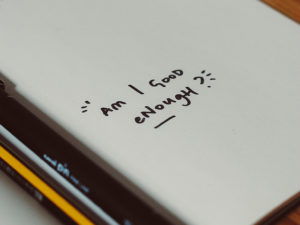 notebook opened to blank page with a scribbled "Am I Good Enough?"